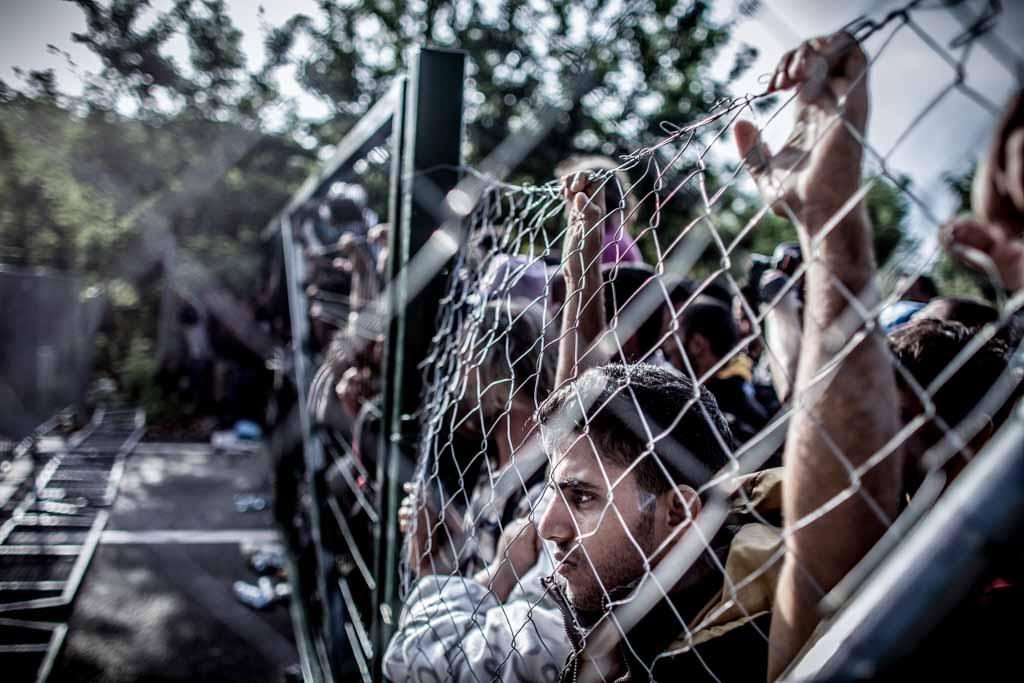 Photo de personnes derrière une barrière métallique. Par Sandor Csudai
